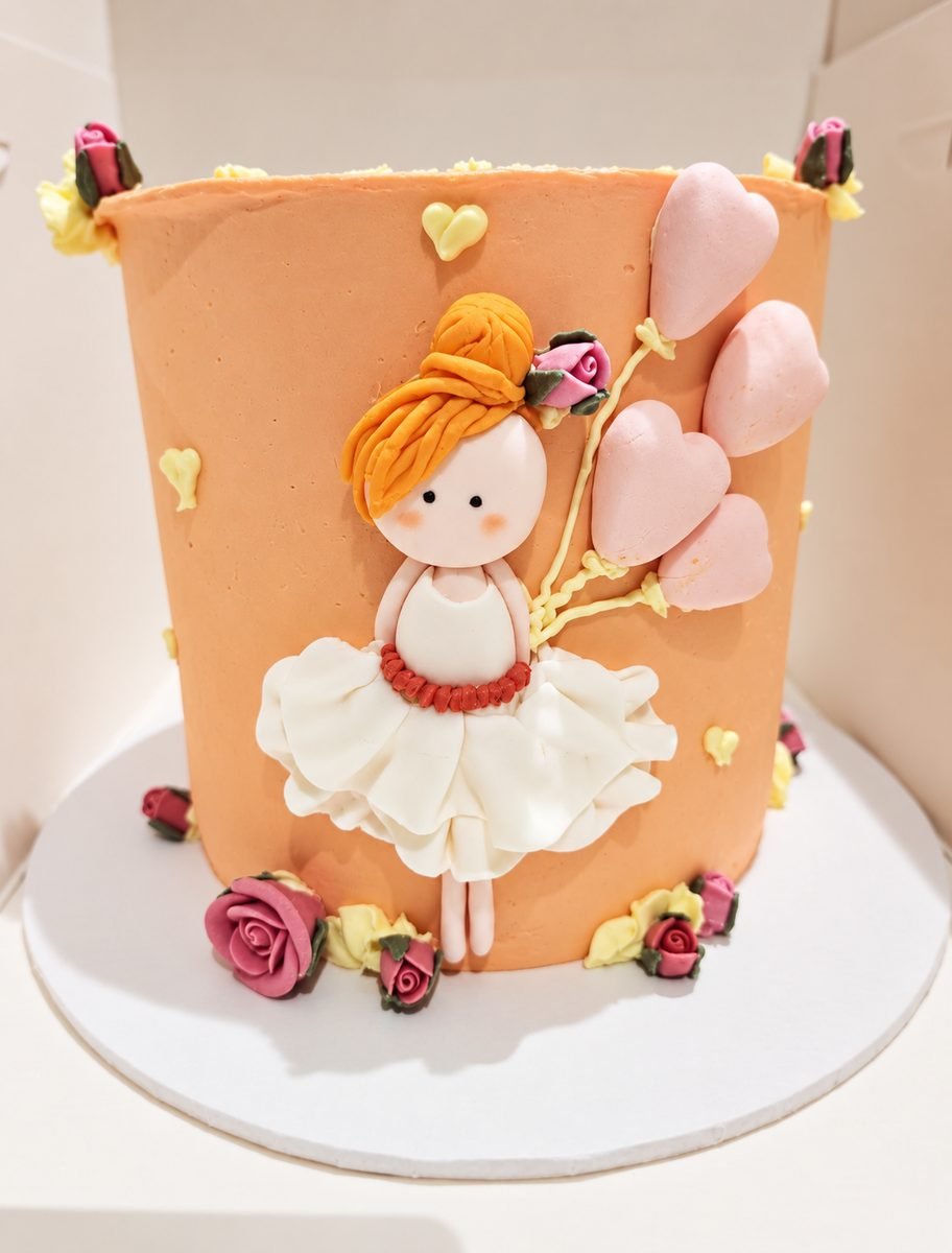 Peach buttercream cake with a fondant ballerina in a white tutu holding pink heart balloons, trimmed with piped roses