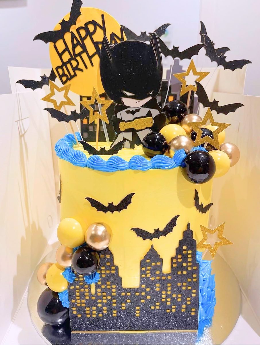 Batman birthday cake with a yellow drip, black bat silhouettes, a Gotham skyline panel and gold and black chocolate spheres