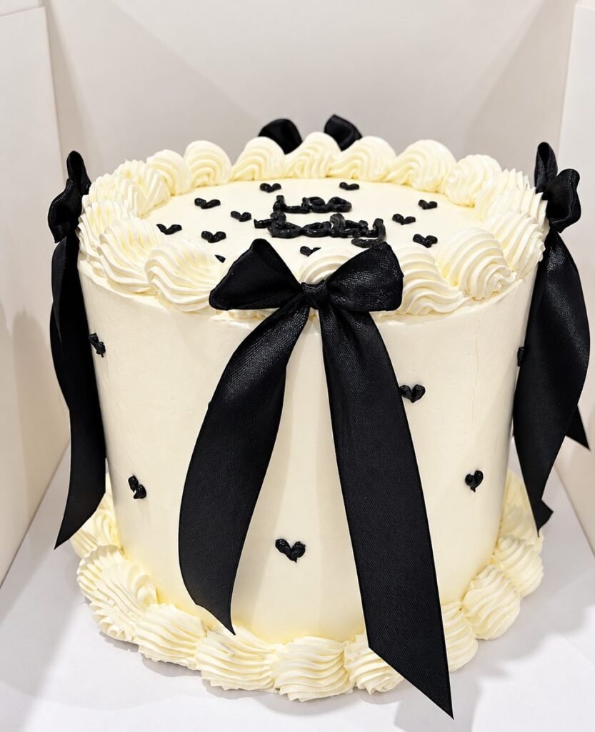 Cakes gallery: Tall cream buttercream cake with piped shell borders, black satin bows and small black piped hearts