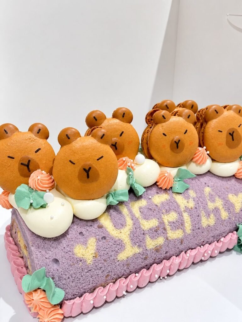 Purple roll cake topped with bear-face macaron shells, buttercream rosettes and piped lettering