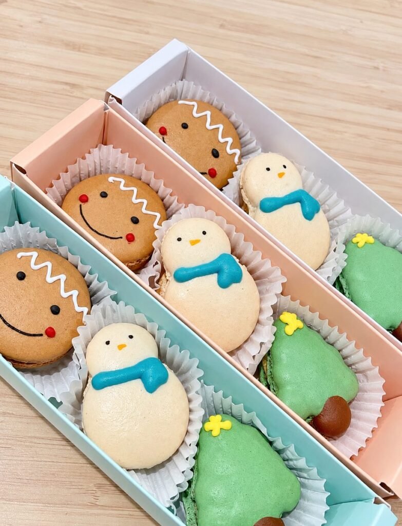 Three gift boxes each holding a gingerbread man, snowman and Christmas tree macaron