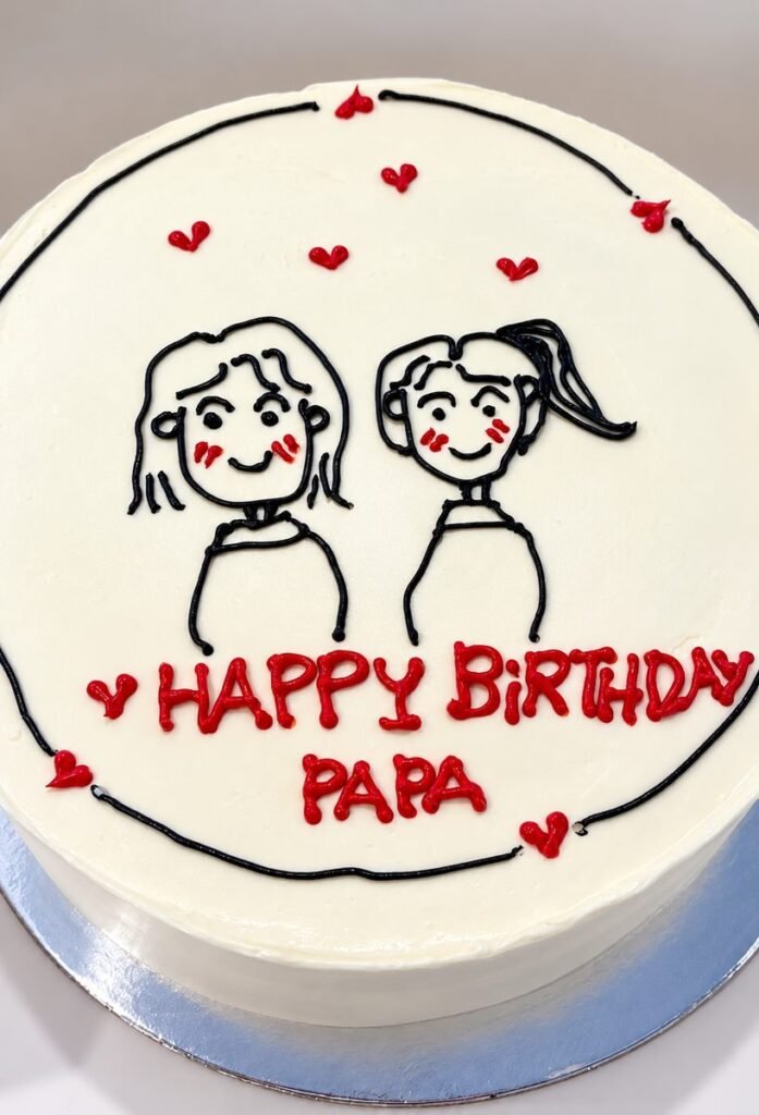 White cake piped with a hand-drawn style portrait of two girls, red hearts and the words happy birthday papa