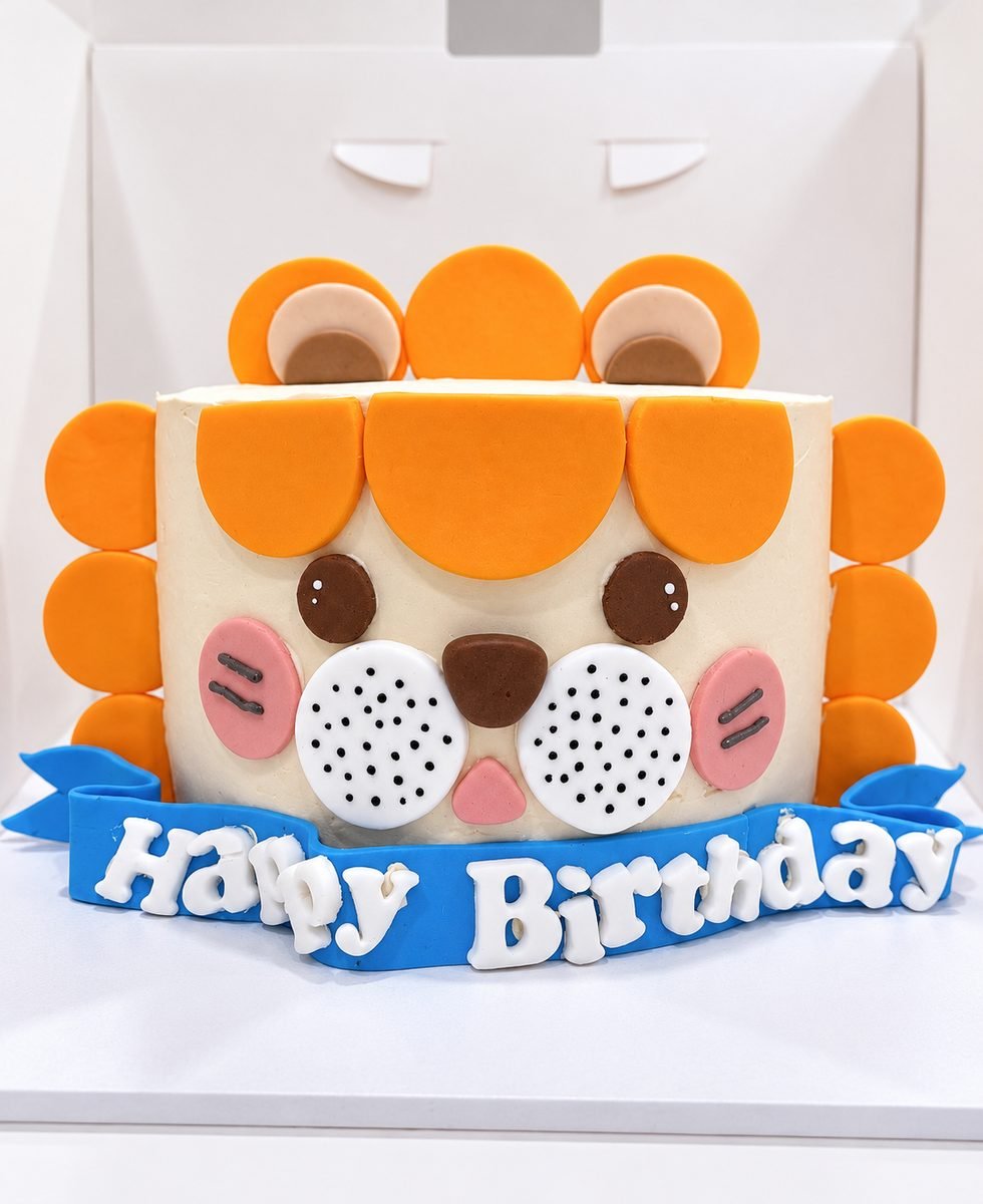 Lion face birthday cake in cream buttercream with an orange fondant mane and a blue Happy Birthday banner