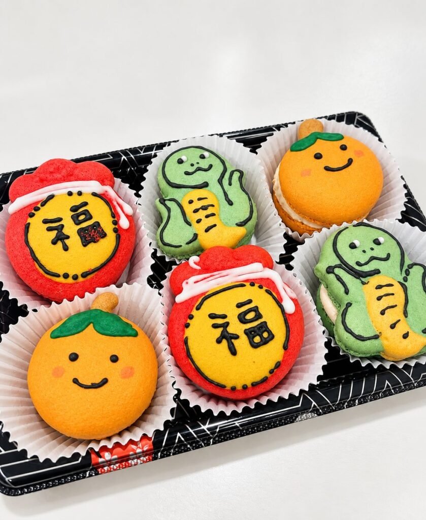 Box of Lunar New Year macarons shaped as red fortune bags with the character 福, green snakes and smiling mandarins