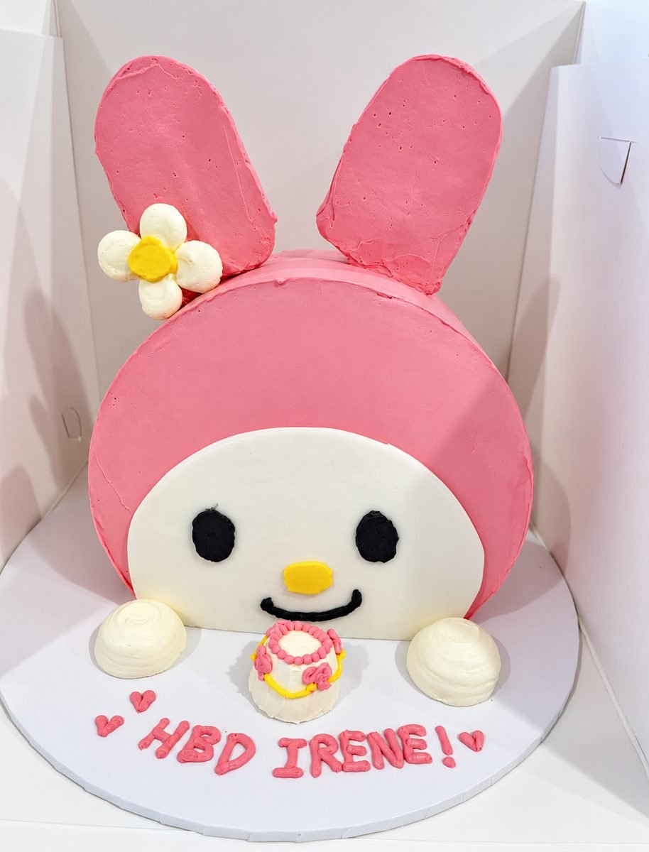 Pink and white character cake shaped as a bunny face with tall ears, a meringue flower and piped birthday lettering