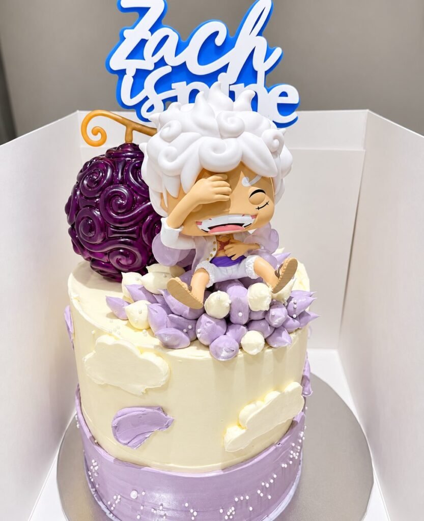 Cream and lilac two-tier birthday cake topped with a Luffy figure and purple devil fruit