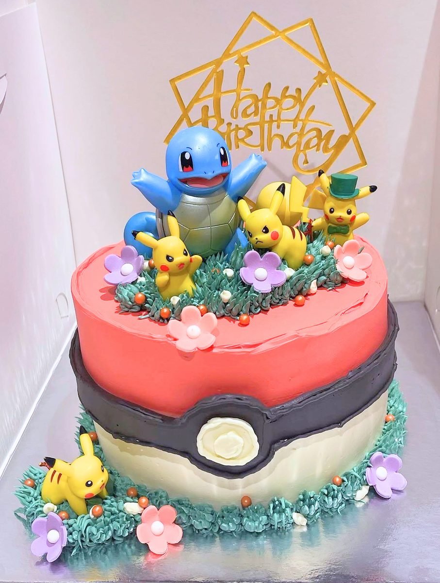 Pokeball birthday cake in red, black and white buttercream with Pikachu and Squirtle figurines on piped green grass and flowers