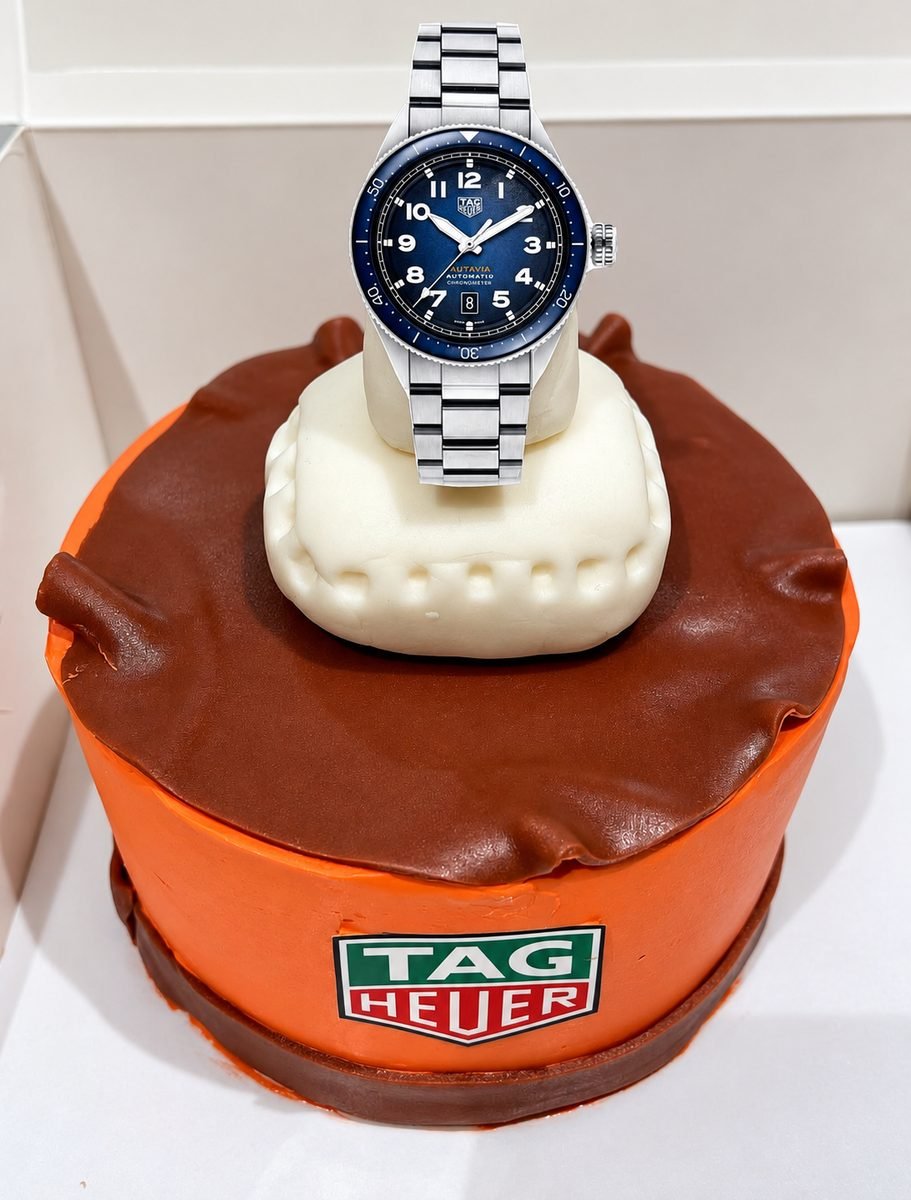 Novelty watch-box cake in orange and brown fondant with a TAG Heuer motif and a watch displayed on a fondant cushion